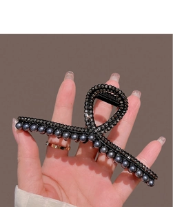 Detail of black shark hair claw with rhinestones and grey pearls held in hand