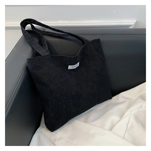 Close-up of black corduroy tote bag showing ribbed texture and white fashion label