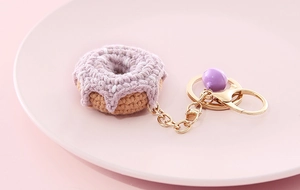 Macro shot of handmade purple crochet donut keychain with bell on pink plate