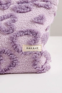 Close-up of soft purple plush makeup bag fabric with textured pattern and H&R BAG logo