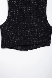 Gros plan du tissu en tweed noir avec fils métalliques et détails de l'ourlet du gilet