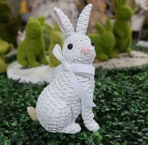 Close-up of white resin rabbit with woven texture and satin bow on green grass