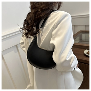 Fashionable black crescent shoulder bag shown on model wearing a white blazer