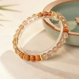 Détail du bracelet zen avec perles de bois brun et agate grise sur fond de sable