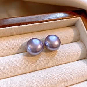 Detailed macro view of smooth purple round pearl earrings in a beige jewelry display tray