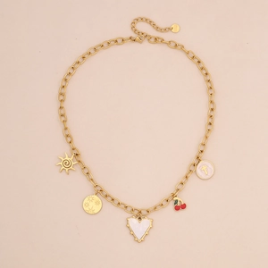 Dettaglio collana in acciaio dorato con ciondoli a cuore e ciliegia su sfondo beige