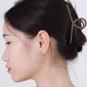 Gros plan de créoles torsadées en or rose et d'une pince à cheveux mate sur un modèle