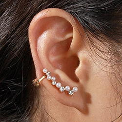 Macro view of gold curved ear cuff with alternating white pearls and clear rhinestones