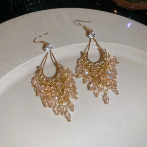 Detail of elegant gold drop earrings with champagne crystals and tassels on ceramic plate