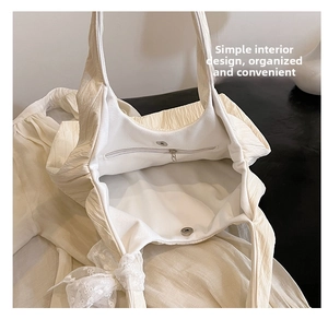 Close-up of off-white pleated tote bag showing interior zip pocket and magnetic buckle