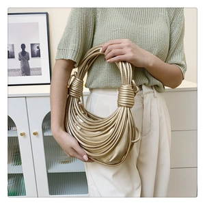 Detail shot of a golden knotted underarm bag with metallic texture on a model