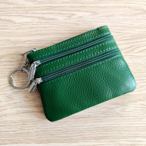Green genuine leather mini coin purse with three zipper compartments and keychain on wood