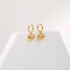 Close-up of golden 18K brass heart pendants on hoops displayed on a geometric stand