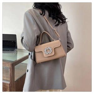 Détail du sac beige avec boucle en cristal porté par une femme en tailleur gris