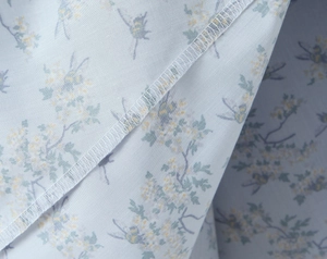 Detailed close-up of light blue floral fabric edges with white lockstitch sewing