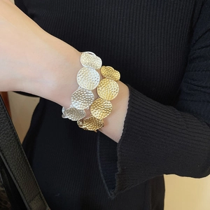 Detail of gold and silver textured metal disk bracelets on a black ribbed sleeve