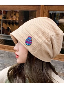 Detail of colorful Easter enamel pin on a beige knitted beanie with Happy Easter text