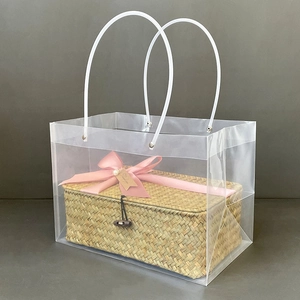 Transparent PVC gift bag with white tube handles showing a woven grass basket inside