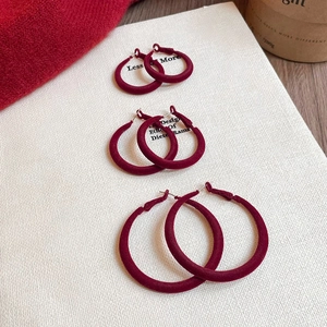 Three sizes of burgundy flocked hoop earrings arranged vertically on white textured paper