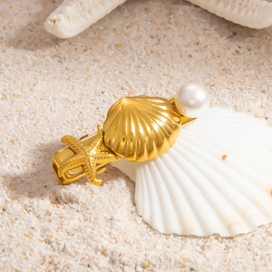 Detail of a 18k gold starfish hair clip with a pearl on a white shell and sand