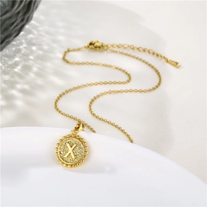 Close-up of golden round pendant with letter X and small bead details on a white plate