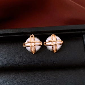 Macro detail of gold-plated geometric square earrings with pearl inlay on black padding