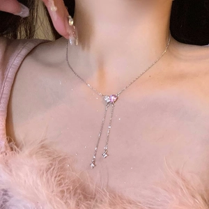 Dettaglio di una collana con nappine e cristalli a cuore rosa e bianchi sulla clavicola