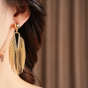 Close-up of golden tassel earrings with round stud and delicate bead chains on a model