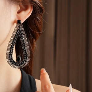 Close-up of black oversized water-drop earrings featuring micro-pave crystals on a model
