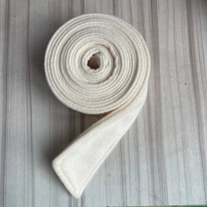 Close-up of a white wool felt belt roll with a thick fiber texture on a wooden background