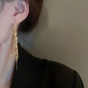 Detail of long gold tassel leaf earrings worn by a model against a black outfit