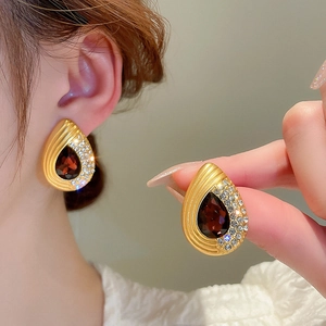 Detail of gold teardrop earrings featuring a deep red gemstone and white rhinestones