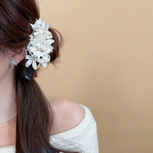 Detail of white fabric flower hair claw clip worn by a model in a sweet and elegant style