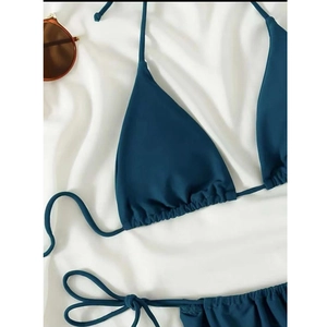 Flat lay of a dark blue triangle bikini set with side ties and sunglasses on white silk