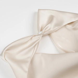 Macro shot of elegant champagne satin halter dress featuring a knotted button detail