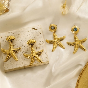 Detailansicht von goldenen Seestern-Ohrringen mit Muscheltextur und Perlmutt-Inlay