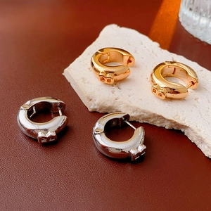 Detailed view of gold and silver circular hoop earrings with letter B on leather background