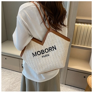Detailed close-up of woven straw tote bag with brown leather trim and MOBORN PARIS embroidery