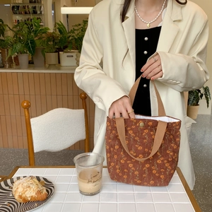 Detail of red-brown floral corduroy handbag with magnetic clasp in a cozy cafe setting