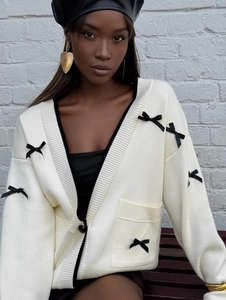 Dettaglio ravvicinato di cardigan bianco in maglia con fiocchi neri e scollo a V