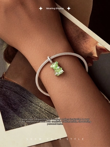 Detailed close-up of a silver mesh bracelet with a green translucent bear charm on a wrist