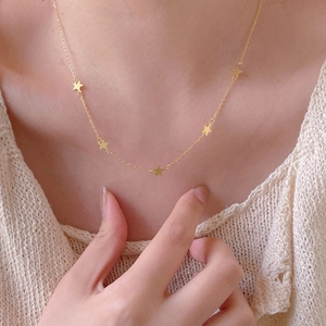 Detailed view of a gold star necklace with five pendants worn over a beige sweater