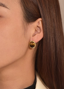 Close-up of a model wearing round tiger eye stud earrings with a gold-plated setting