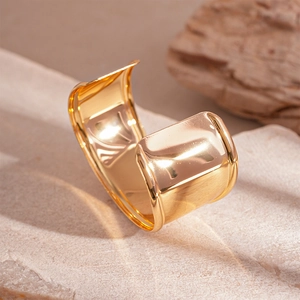 Detailed close-up of wide polished gold open cuff bracelet on a stone and wood background