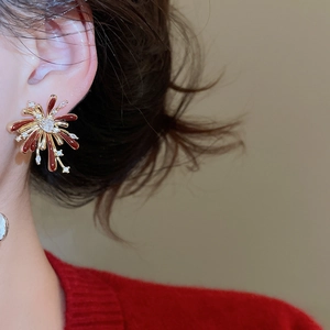 Detailed close-up of firework-shaped gold earrings with red enamel and crystals