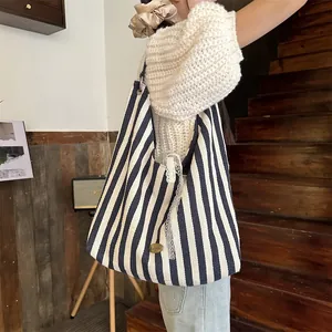 Détail d'un sac cabas en toile rayée avec dentelle et logo vintage porté à l'épaule