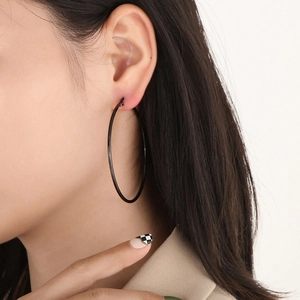 Close-up of large black stainless steel hoop earring worn by a model in a minimalist style
