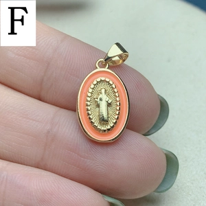 Macro detail of oval Jesus pendant with orange enamel edge and gold plating