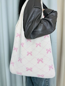 Close-up of cream knitted tote bag featuring pink bow patterns and woven textures