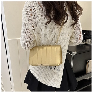 Fashionable golden quilted crossbody bag with metal chain strap worn on woman's shoulder
